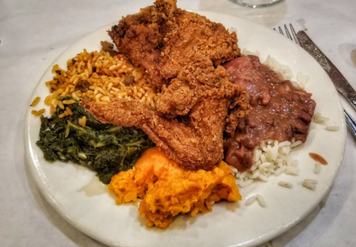 A plate of food featuring fried chicken, rice, refried beans, collard greens, and sweet potato mash.