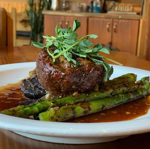 A plated dish featuring a beef filet topped with microgreens, served with asparagus and a savory sauce.