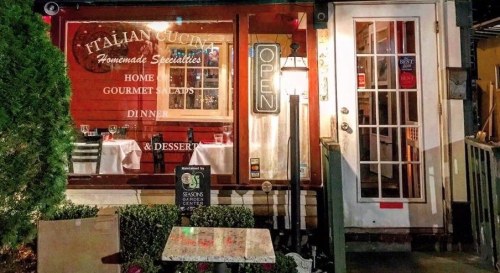 A cozy Italian restaurant exterior at night, featuring an "Open" sign and a welcoming entrance with outdoor seating.