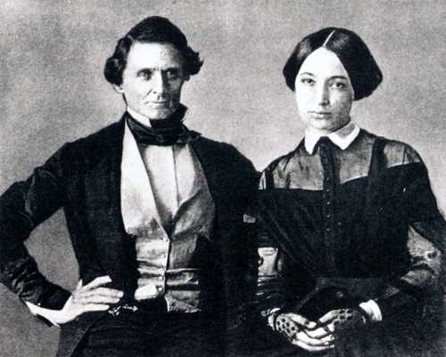 A historical black-and-white portrait of a man and woman, both dressed in 19th-century attire, posing together.