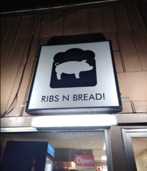 Sign for "Ribs N Bread!" featuring a pig silhouette and a bread icon, illuminated at night.