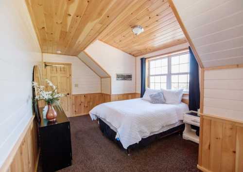 Cozy bedroom with wooden walls, a large window, a bed, and a dresser, featuring warm, inviting decor.