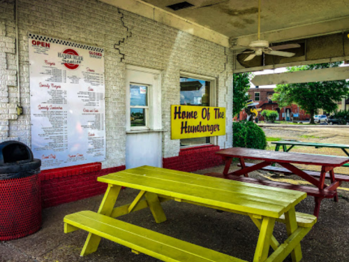 A colorful outdoor dining area with yellow picnic tables and a menu board at a hamburger restaurant.