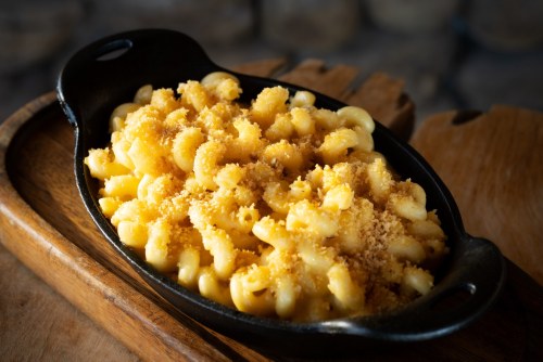 A serving of creamy macaroni and cheese topped with golden breadcrumbs, served in a black dish on a wooden board.