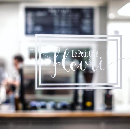 A café window with the sign "Le Petit Café" and a blurred figure in the background.