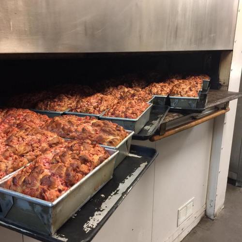 Several trays of cooked meatloaf lined up in an industrial oven, with a golden-brown crust on top.
