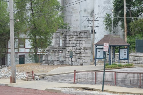 Ruins of a stone structure beside a road, with trees and power lines in the background. No parking sign visible.