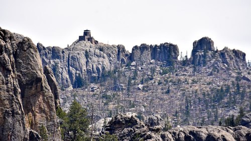 A rocky landscape with a distant lookout tower atop a mountain, surrounded by sparse trees and rugged terrain.