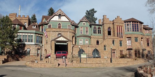 A large, historic stone mansion with various architectural styles, surrounded by trees and a circular driveway.