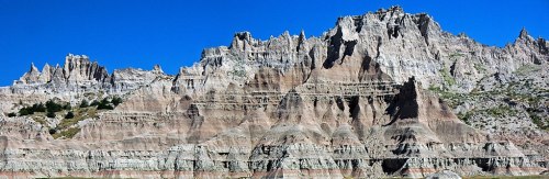 A panoramic view of rugged, layered rock formations under a clear blue sky.
