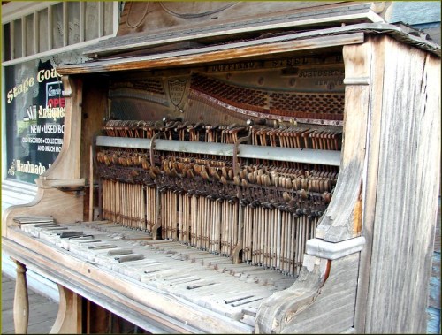 An old, weathered player piano with exposed mechanisms and wooden casing, showcasing its vintage charm.