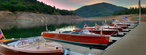 A serene lakeside scene with vintage wooden boats docked at a pier, surrounded by lush green hills and a colorful sunset.