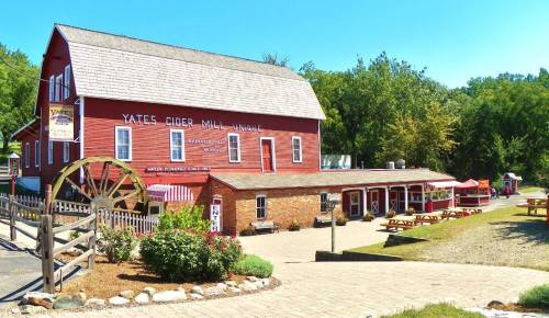 A red barn-style building with a sign for Yates Cider Mill, surrounded by trees and outdoor seating areas.