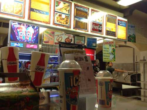 A concession stand with menus, drinks, and snacks visible, featuring colorful signage and a busy atmosphere.