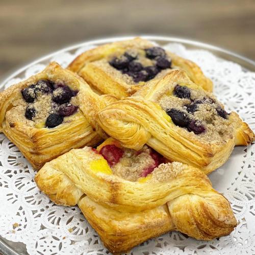 A plate of flaky pastries filled with mixed berries and topped with crumbly streusel, arranged on a lace doily.