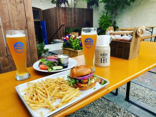 Two glasses of beer, a plate of fries, a burger with toppings, and a side salad on a wooden table outdoors.