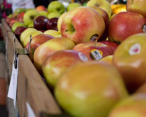 A close-up of a wooden crate filled with various apples at a market, showcasing their vibrant colors and labels.