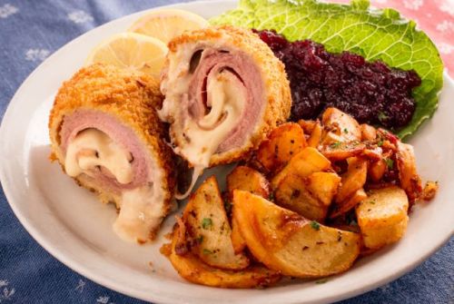 A plate featuring a sliced, breaded meat roll with cheese, served with roasted potatoes, lettuce, and cranberry sauce.