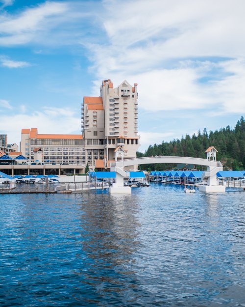 A waterfront view of a hotel with a marina, surrounded by trees and a blue sky with clouds.