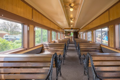 Interior of a vintage train car featuring wooden benches and large windows, with a warm, inviting atmosphere.
