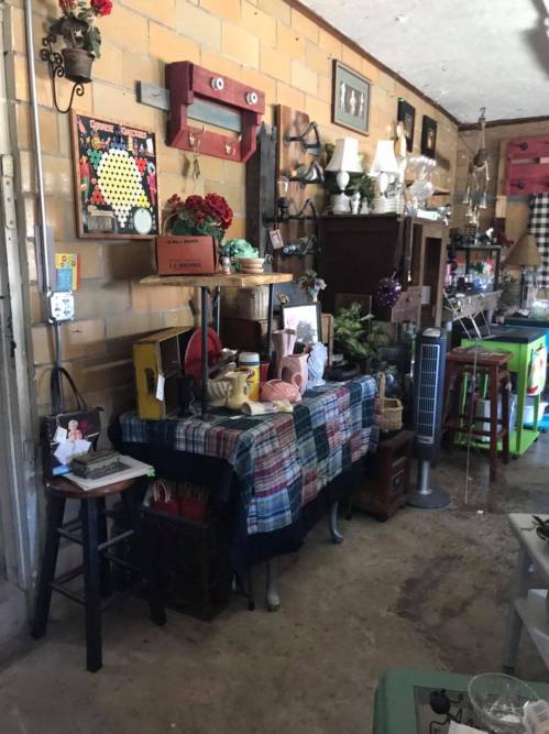 A cluttered room filled with various vintage items, furniture, and decorations against a brick wall.