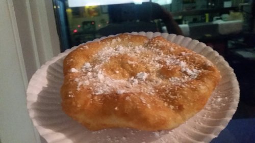 A golden-brown fried pastry dusted with powdered sugar on a white paper plate.
