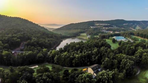 Aerial view of a serene landscape with rolling hills, a lake, and lush greenery at sunrise.