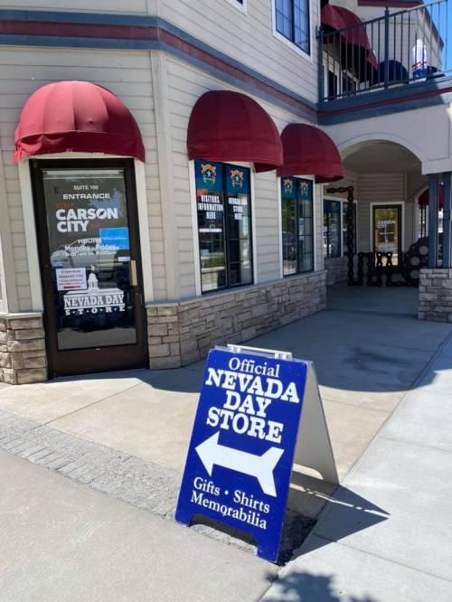 A storefront with a sign reading "Official Nevada Day Store" and red awnings, promoting gifts and memorabilia.