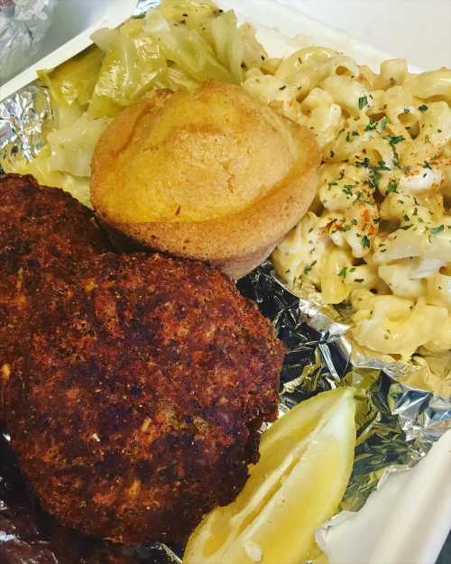 A plate featuring fried chicken, macaroni and cheese, cornbread muffin, sautéed cabbage, and a lemon wedge.