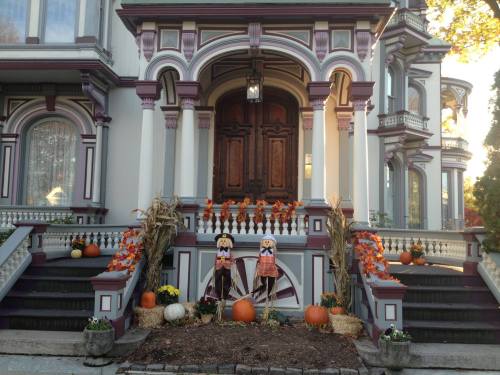 A beautifully decorated house with pumpkins, scarecrows, and autumn leaves on the steps, showcasing a festive fall theme.