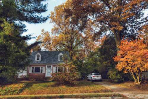 A charming house surrounded by autumn trees with colorful leaves and a car parked in the driveway.