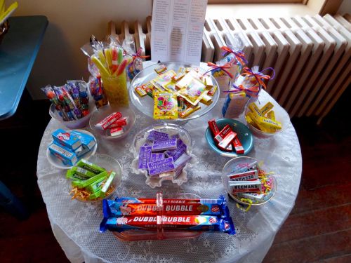 A table covered with a lace cloth displaying various colorful candies and treats in bowls and bags.