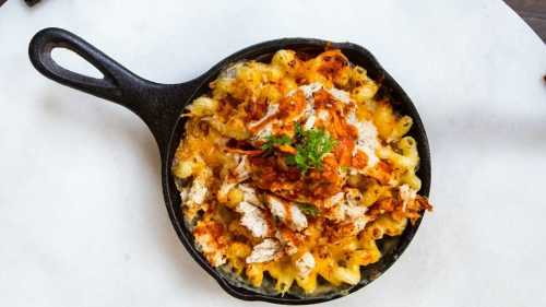 A cast-iron skillet filled with creamy pasta topped with shredded chicken and a golden, crispy layer.