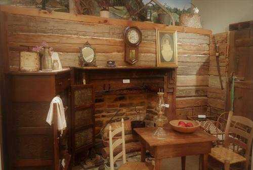 Cozy rustic room with a wooden fireplace, vintage furniture, and decorative items on the walls and shelves.
