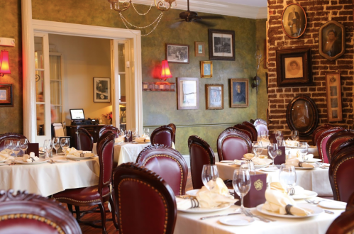 Elegant restaurant interior with wooden tables, red chairs, and vintage wall decor, creating a warm, inviting atmosphere.