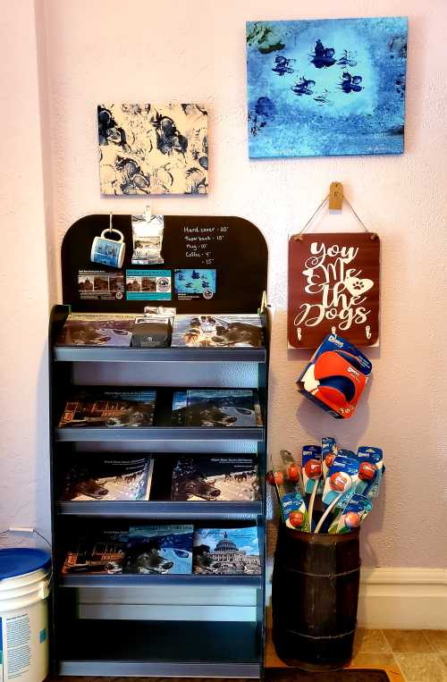 A display shelf with books and dog toys, featuring wall art and a sign that says "You & Me & Dogs."