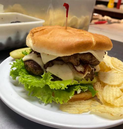 A juicy burger with lettuce, cheese, and bacon on a bun, served with a side of potato chips.