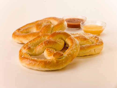 Three soft pretzels with dips in the background: one plain, one with salt, and one with a sweet glaze.