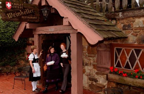 Three women stand at the entrance of a rustic restaurant, smiling and holding food, with flowers in the foreground.