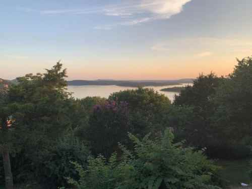 A serene landscape view of a lake at sunset, surrounded by trees and hills under a colorful sky.