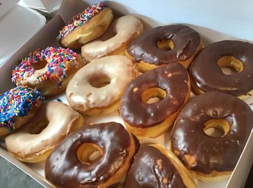 A box of assorted donuts, featuring chocolate, glazed, and sprinkles on a blue frosted donut.