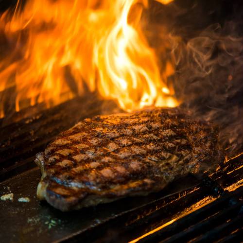 A perfectly grilled steak sizzling on a hot grill, with flames and smoke rising around it.