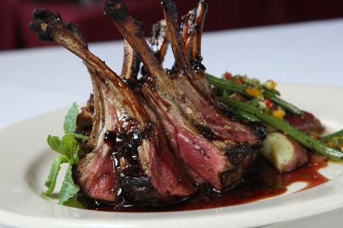 A plate of grilled lamb chops with a rich sauce, served with green beans and colorful vegetables.