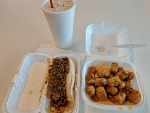 A takeout meal featuring a sandwich, a container of chicken bites with cheese, and a drink in a cup.