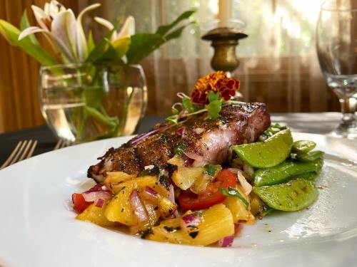 A beautifully plated dish featuring grilled steak, pineapple salsa, and sautéed snap peas, with a floral centerpiece in the background.