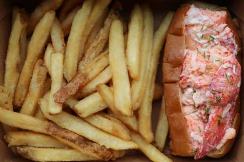 A lobster roll filled with lobster meat, served alongside a generous portion of golden French fries.