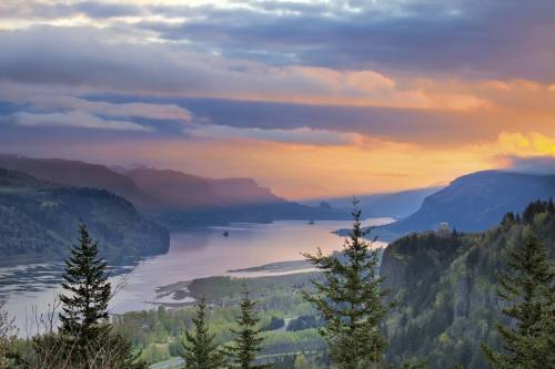 A scenic view of a river winding through mountains at sunset, with colorful clouds and lush greenery in the foreground.