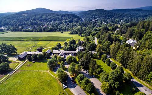 Aerial view of a lush green landscape with trees, fields, and a small cluster of buildings nestled in the hills.