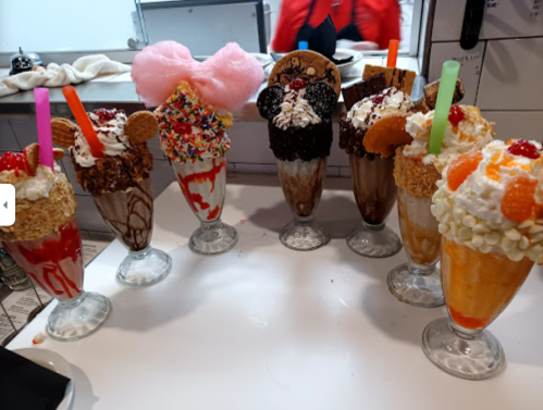 A colorful array of extravagant milkshakes topped with candy, whipped cream, and various treats in tall glasses.