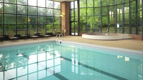Indoor swimming pool with large windows, lounge chairs, and a hot tub surrounded by greenery.